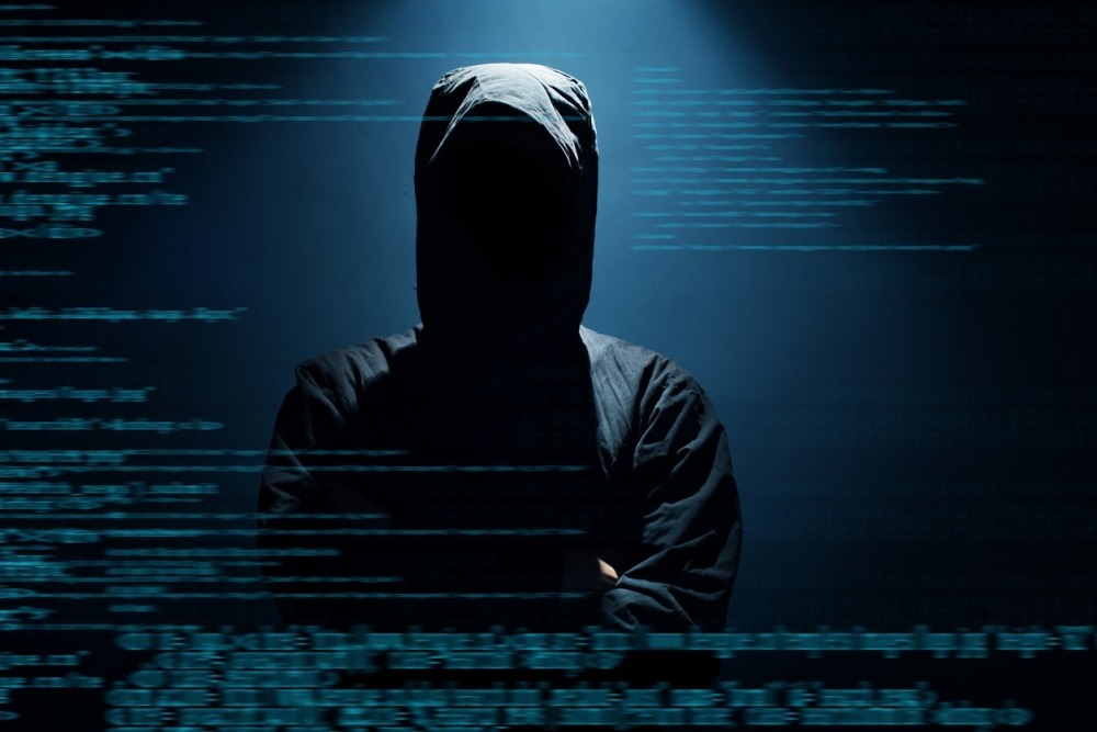 Potential hooded hacker wearing all black with binary background