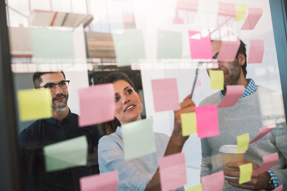 Diverse group of businesspeople brainstorming with colorful adhesive notes on a glass wall in a bright modern office