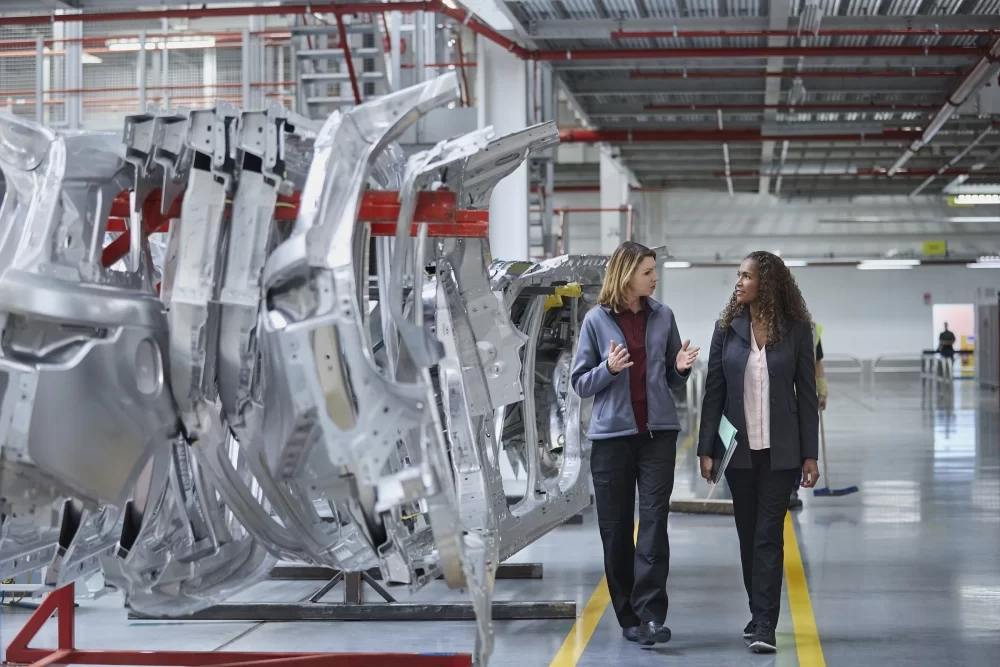 two women walking in automotive manufacturing plant discussing quality management in automotive industry