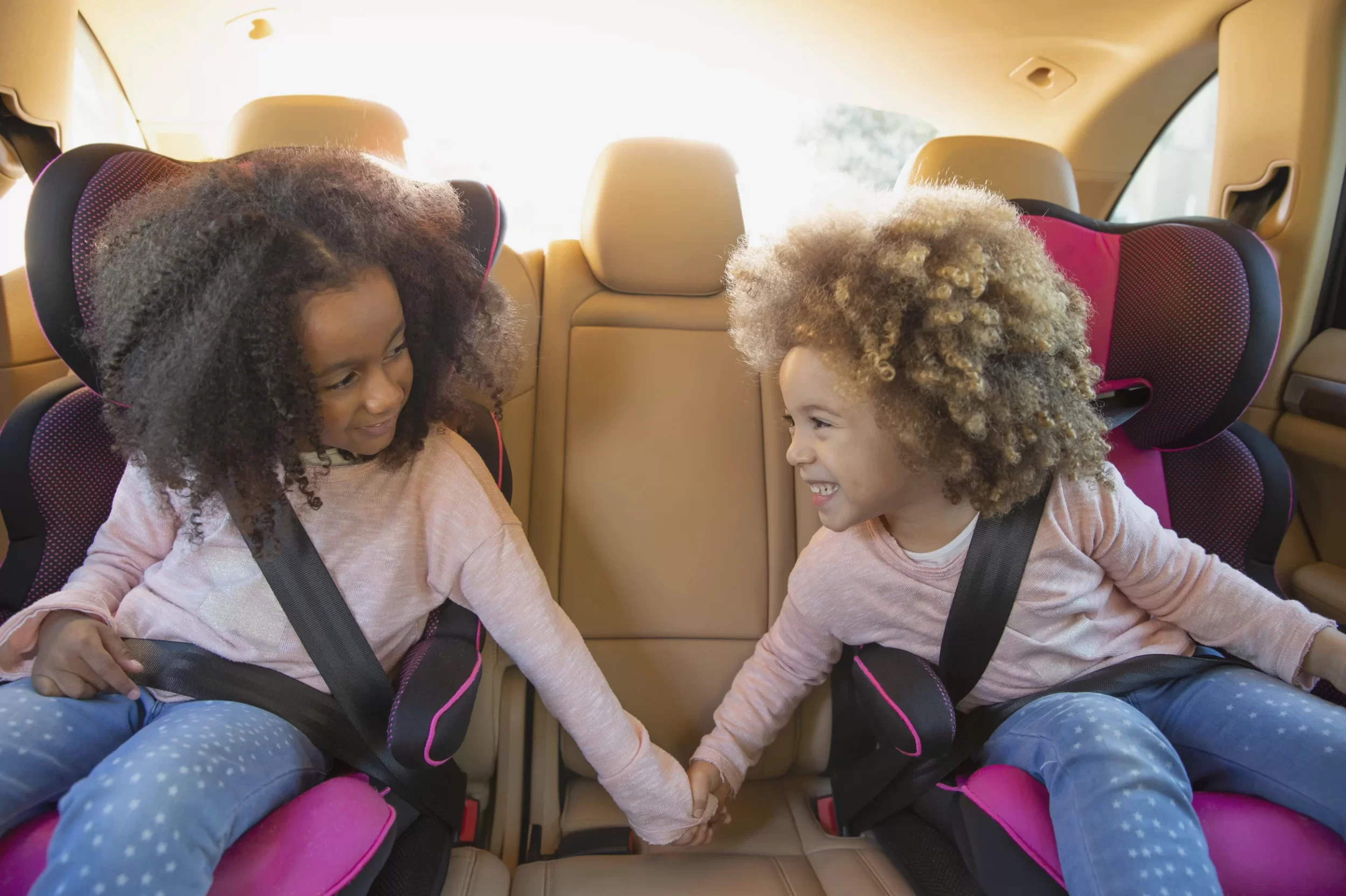 Two little girls in child seats holding hands and smiling in back seat of car