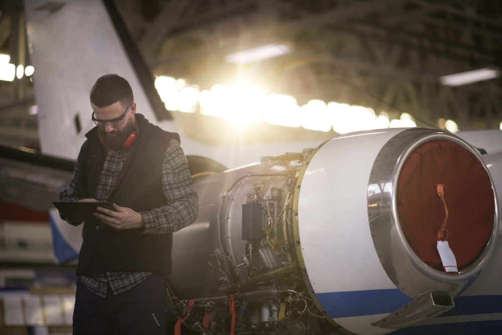 Male aircraft engineer holding a digital tablet that's running ETQ Reliance AS9100 quality management system to ensure aerospace quality